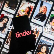 phone with black and pink tinder logo in front of backdrop of various tinder profiles