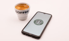 Starbucks logo on an iPhone next to a cup of coffee