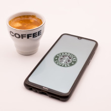 Starbucks logo on an iPhone next to a cup of coffee