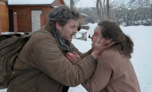 A man embraces a girl with blood on her face outside in the snow.