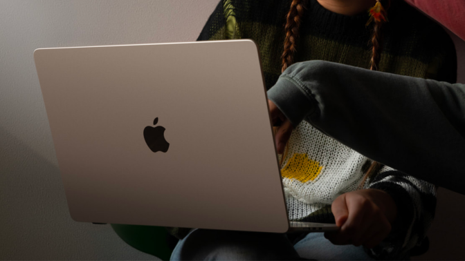 a close-up of a woman holding a 15-inch apple macbook air while another person points at its screen