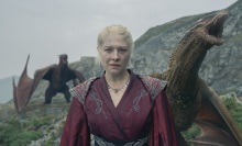 Rhaenyra stands on the island of Dragonstone, backed by two dragons.