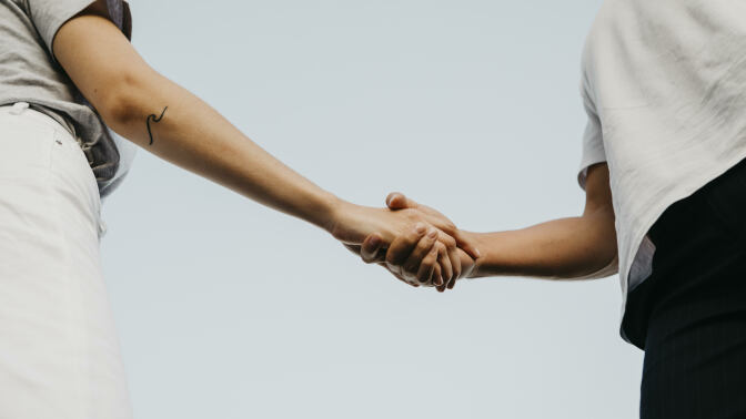 Two people shaking hands against the blue sky. 