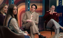 A group of men and women sit on stage at a late night show.