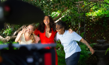 Gallo, Roth Weigel, and Wall hold onto each other and laugh while behind a large film camera.