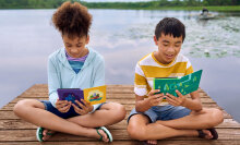 Two kids sit by the water reading their Kindles