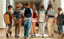 a group of school kids walk down the hallway while all wearing backpacks