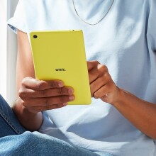 a yellow onn. tablet held by someone wearing a blue shirt and jeans while sitting next to a window