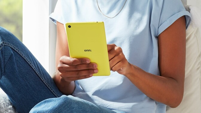 a yellow onn. tablet held by someone wearing a blue shirt and jeans while sitting next to a window