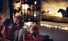 A family is watching a movie on a wall thanks to a projector