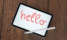 Apple iPad mini sitting on a table with the word "hello" written in red by a stylus pen.