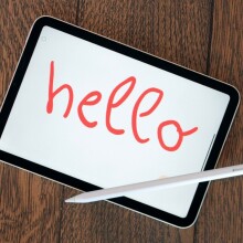 Apple iPad mini sitting on a table with the word "hello" written in red by a stylus pen.