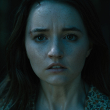 A close-up of a woman looking scared in a dark room.