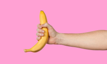 An outstretched arm holds a banana on a pink background