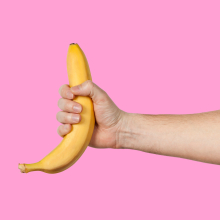 An outstretched arm holds a banana on a pink background