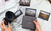 Person's hands using mirrorless camera and portable photo printer with scattered printed photos and fabric in peripherals