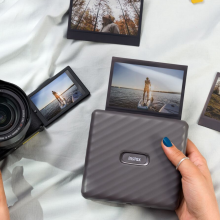 Person's hands using mirrorless camera and portable photo printer with scattered printed photos and fabric in peripherals