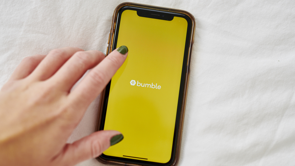 A hand over a smartphone displaying the Bumble logo. 