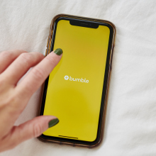 A hand over a smartphone displaying the Bumble logo. 