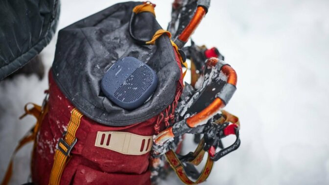 bose soundlink micro bluetooth speaker sits on top of a backpack placed in the snow