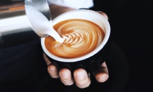 A milk jug being poured into a latte cup.