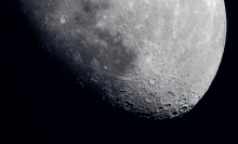 A high contrast, zoomed-in image of the moon. You can make out pits and craters on the moon's surface. 