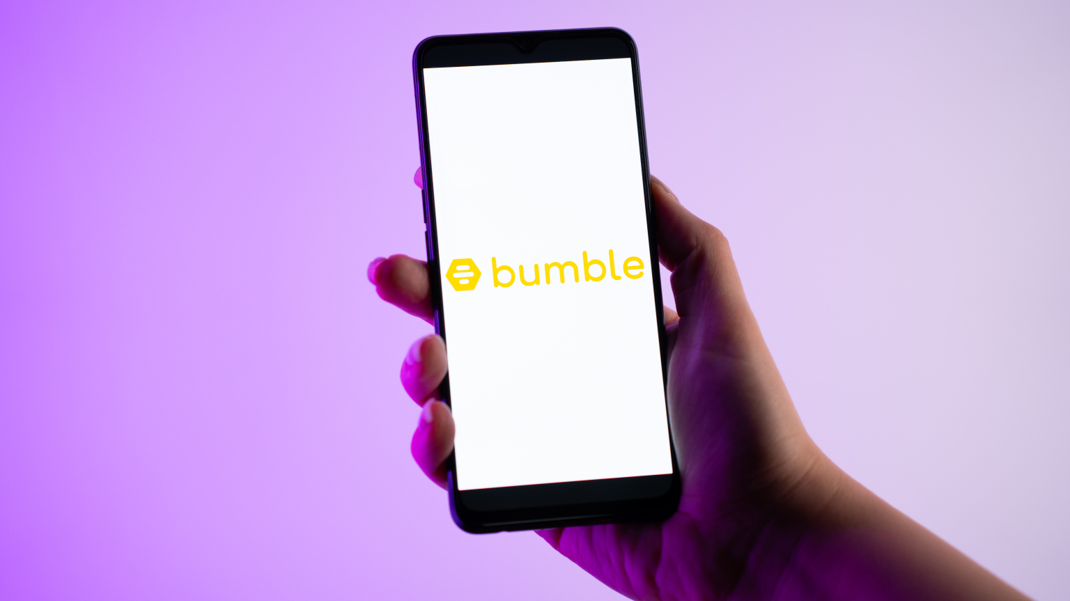 A person is holding a mobile phone with the Bumble dating app logo on its screen