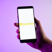 A person is holding a mobile phone with the Bumble dating app logo on its screen