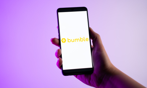 A person is holding a mobile phone with the Bumble dating app logo on its screen