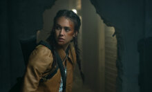 A woman with a bruised face creeps through a dark, abandoned building.