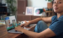 a person sits at a desk with a laptop in front of her while slightly smiling toward the camera