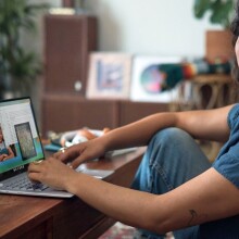 a person sits at a desk with a laptop in front of her while slightly smiling toward the camera