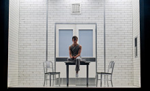 A boy sits in a stark white room on stage in the "Stranger Things" play.