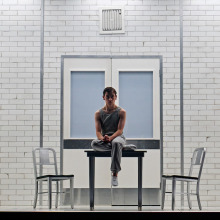 A boy sits in a stark white room on stage in the "Stranger Things" play.