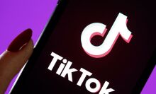 A hand holding a phone displaying the TikTok logo.