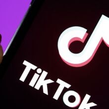 A hand holding a phone displaying the TikTok logo.