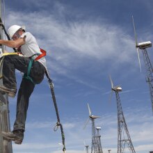 A person climbs down the ladder of a tall wind turbine.