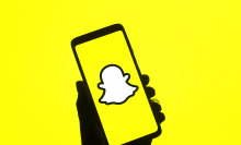 A shadowed hand holds a phone displaying the yellow Snapchat logo.