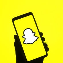 A shadowed hand holds a phone displaying the yellow Snapchat logo.