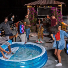 group of people around an inflatable blue pool and two JBL speakers