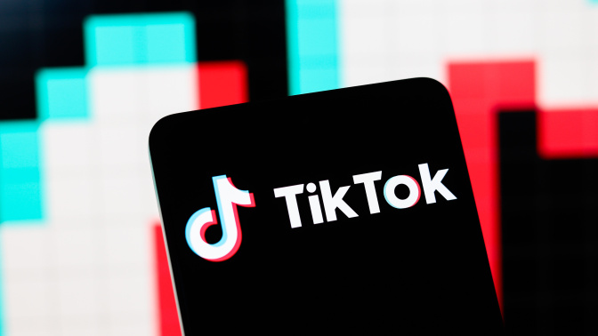 The TikTok logo displayed on a phone with the colors of TikTok, blue and pinkish red in the background.