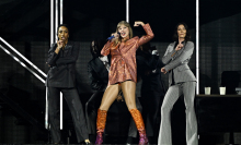 Taylor Swift performing in a blazer with one arm flexed as a demonstration of strength.