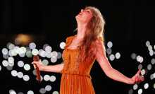 Taylor Swift in an orange dress looking up on stage. 