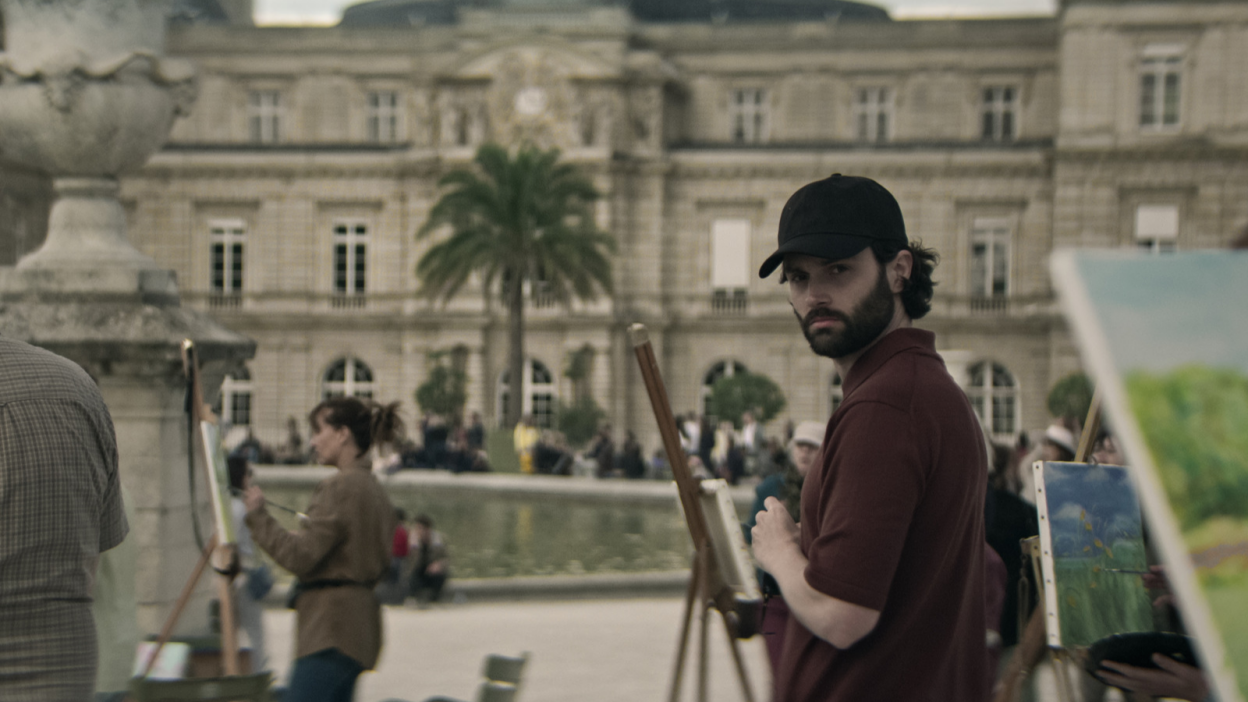 A man stands in a park while people paint. 