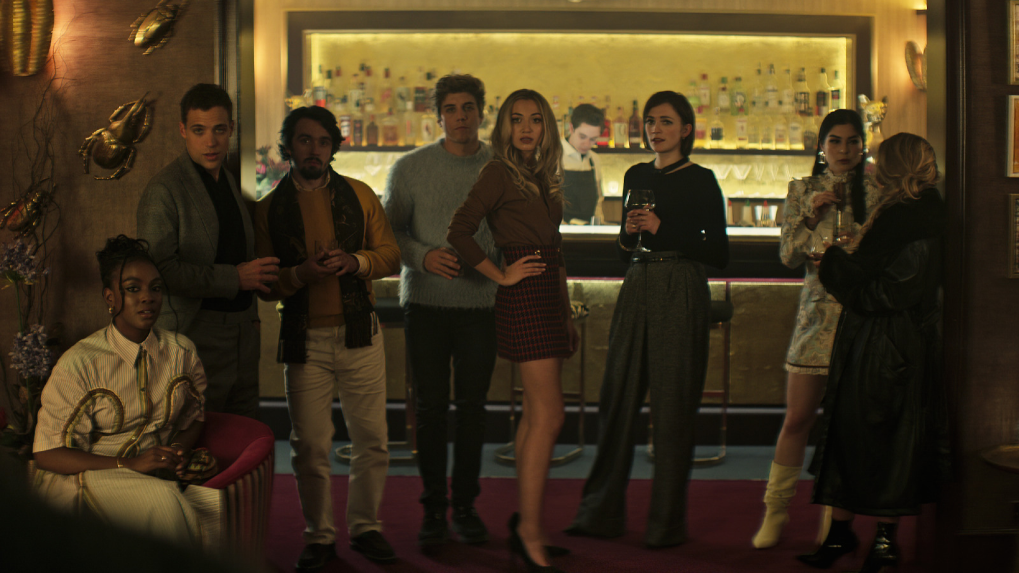 A group of adults in partywear stand in front of a bar. 