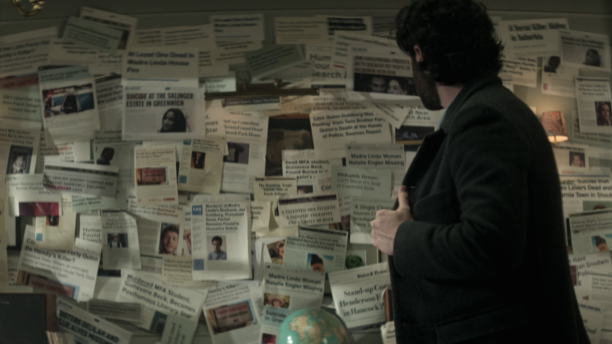 A man stands in front of a board of newspaper clippings. 