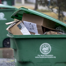 A green recycling bin with the city of Houston logo, full of cardboard boxes. 