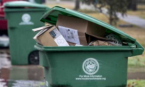 A green recycling bin with the city of Houston logo, full of cardboard boxes. 