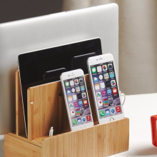 A Macbook, an iPad, and two iPhones sitting in a bamboo organizer and charging station next to a red coffee cup on a desk.