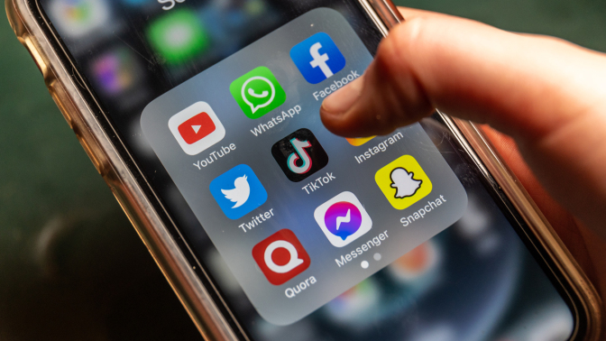 A person using a smartphone has a folder of social media apps open, about to tap TikTok or WhatsApp